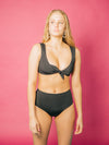 Model wears black tie front closure bikini top. Bikini is made sustainably from recycled fishnets